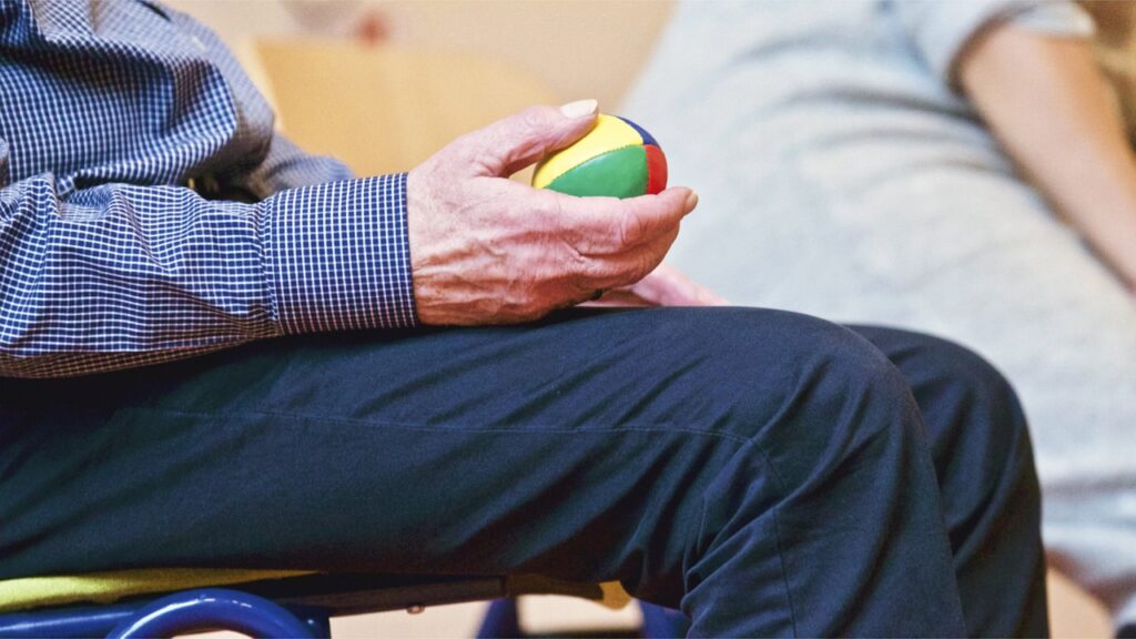 An elderly person sitting on a chair, holding a ball