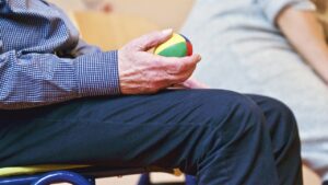An elderly person sitting on a chair, holding a ball