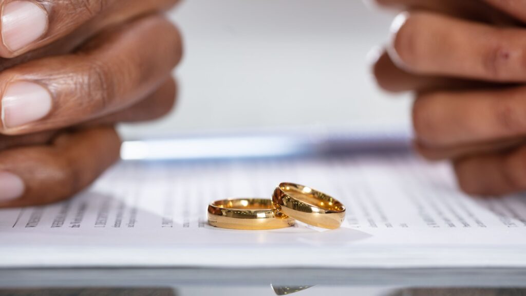 Couple hands on divorce agreement near wedding rings