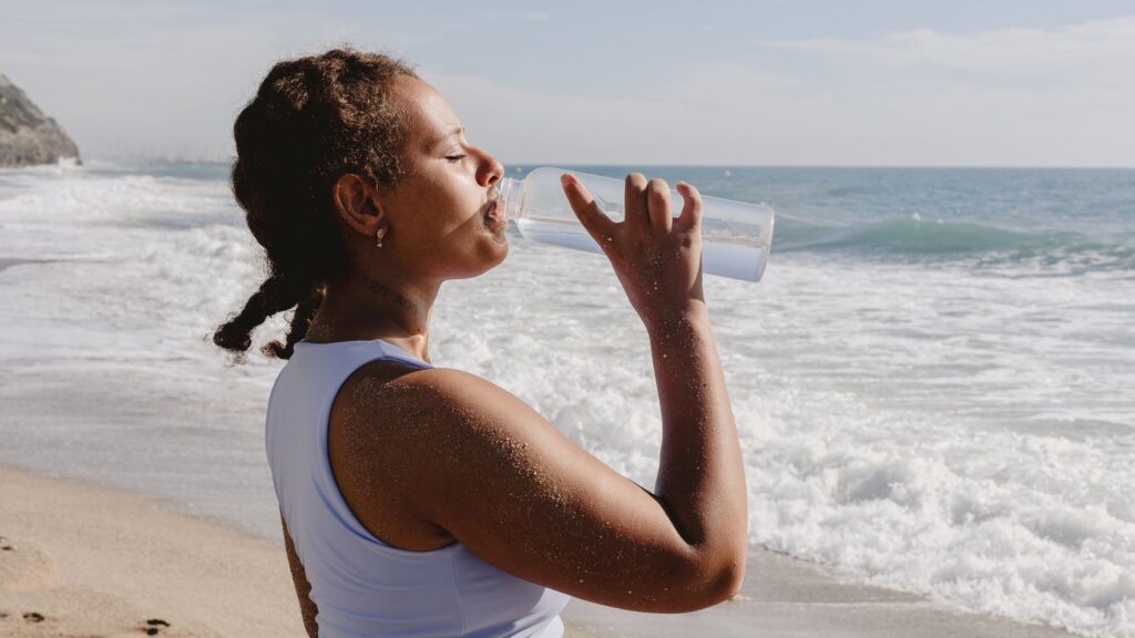 Woman Drinking Water from a Bottle by the Beach